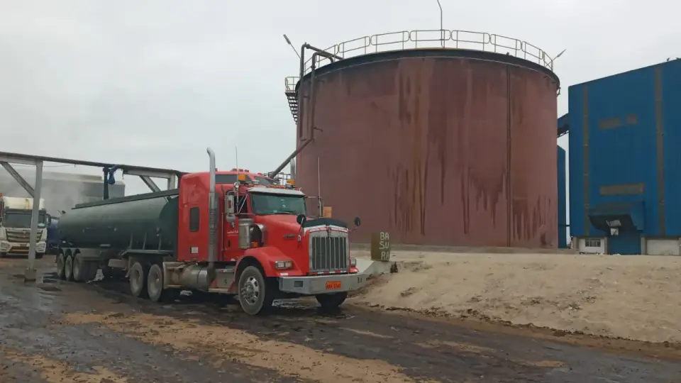 A molasses tanker loading beside a bulk tank streaked with dark molasses