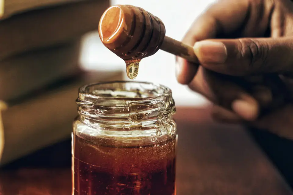 Thick molasses dripping from a dipper into a glass jar